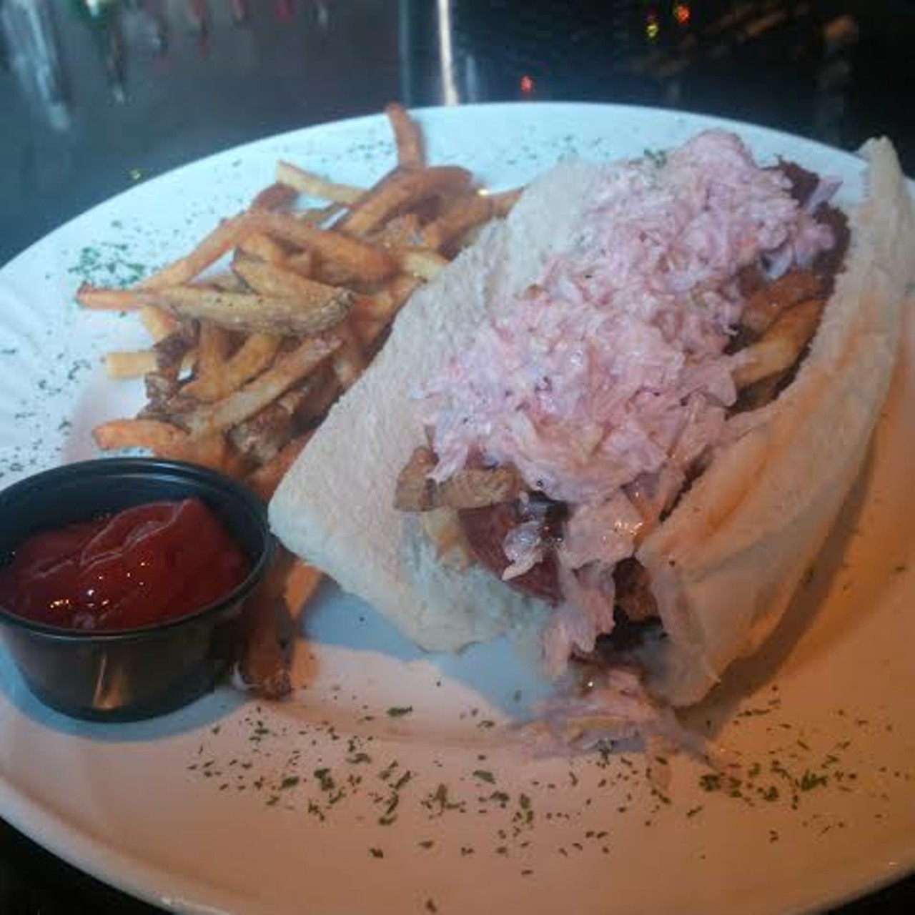 Alligator sausage is topped with French fries, BBQ sauce, and cole slaw resting on a hoagie bun. Try it.