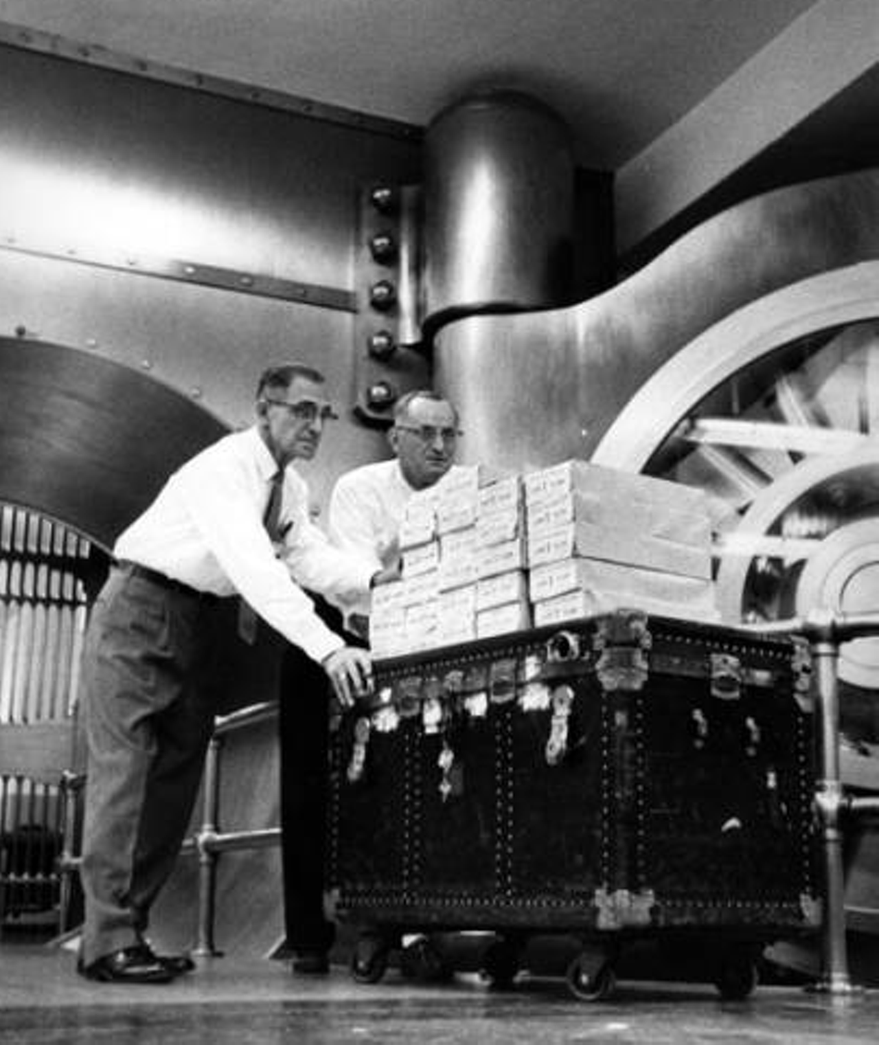 Two bank employees are seen wheeling a trunk into the vault, 1959.
