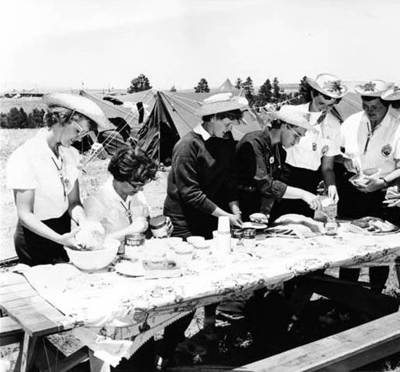 Girl Scouts preparing food at picnic table while camping, 1959.