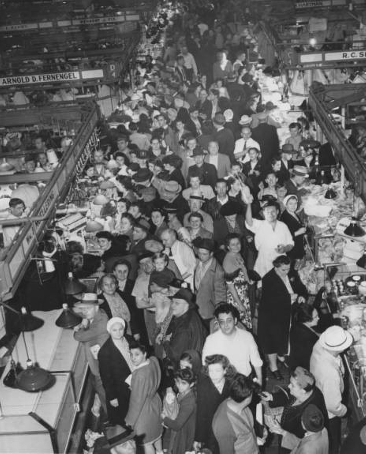 Looking down from balcony towards crowded market floor. Shoppers are looking up to the camera. Visible sign for Arnold D. Fernengel, R. Ashby, Herbert J. Fix, and Wm Moellering.. c. 1946