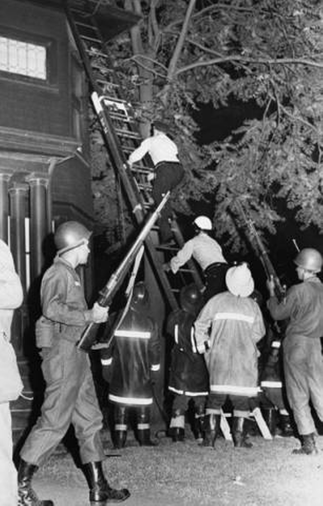 Cleveland firefighters watch as Cleveland police go up a ladder to investigate sniper activity during the 1966 Hough riots. Armed members of the Ohio Army National Guard are also on the scene.