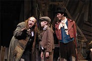 Fagin (George Roth) teaches Oliver (Lincoln Sandham) as the Dodger (Chris McCarrell) watches.