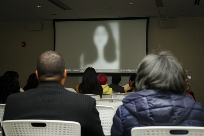 Attendees watch a video of an anonymous Iranian girl, addressing today's violence and injustices. - Mark Oprea